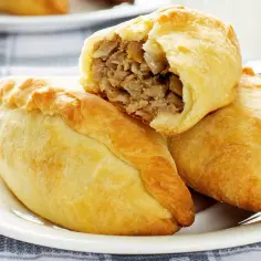Złociste pierogi litewskie z mięsnym farszem, jeden przekrojony, na białym talerzu.