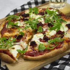 Pikantna nduja pizza z mozzarellą, rukolą i czerwoną cebulą, podana na desce.