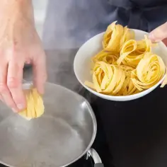 Ręka wkłada porcję tagliatelle do wrzącej wody. Zaczyna się gotowanie makaronu.