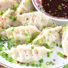 Pyszne pierogi gyoza posypane szczypiorkiem i sezamem, podane z sosem.
