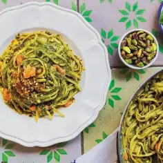 Pyszny makaron po włosku z zielonym pesto, pistacjami i kawałkami łososia na talerzu. Obok miseczka pistacji i listki bazylii.