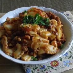Pyszne makaron kolanka w sosie bolońskim, posypane świeżą natką pietruszki.