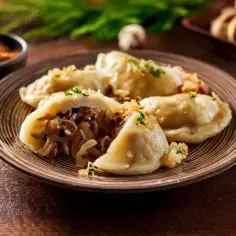 Talerz pełen pysznych, domowych pierogów z kapustą, posypanych szczypiorkiem i skwarkami. Obok czosnek i pieprz.
