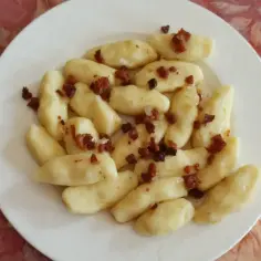 Kopytka przepis podstawowy: pyszne, domowe kopytka z chrupiącym boczkiem na białym talerzu.