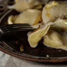 Talerz z pysznymi, domowymi pierogami chłopskimi, polanymi tłuszczem i okrasą. Obok widelca.