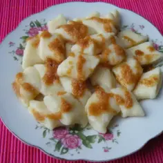 Pyszne kluski leniwe z ziemniakami, polane okrasą, na talerzu z różanym wzorem.