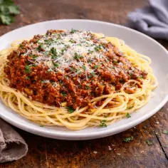 Pyszne spaghetti z bogatym sosem bolońskim, posypane startym serem i świeżą natką pietruszki. Idealne danie dla miłośników włoskich smaków.