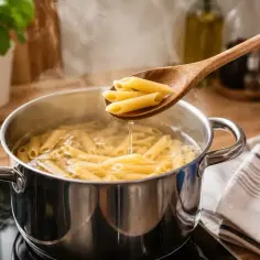 Jak ugotować makaron? Penne w garnku z wrzącą wodą, sprawdzane drewnianą łyżką.