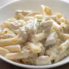 Penne z kurczakiem w kremowym sosie, udekorowane gałązką ziół. Pyszne danie, które zachwyci każdego miłośnika makaronu z kurczakiem w sosie śmietanowym.