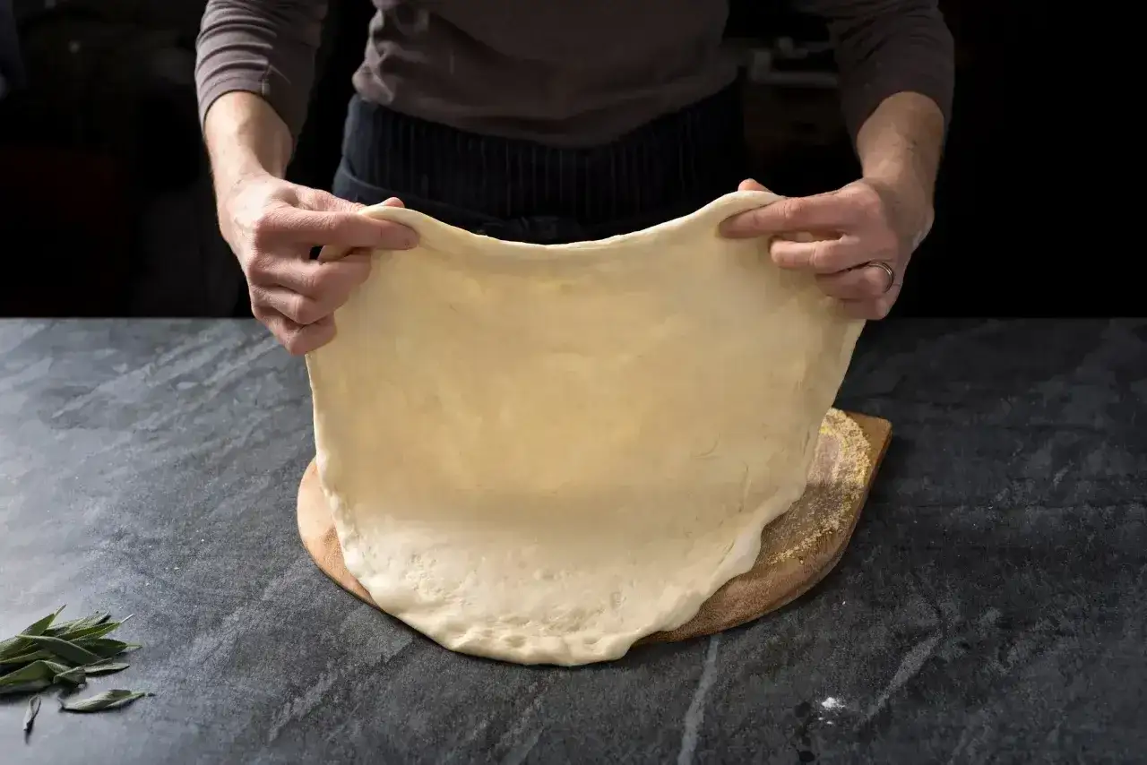 Ręce rozciągają elastyczny, jasny spod do pizzy nad drewnianą łopatą.
