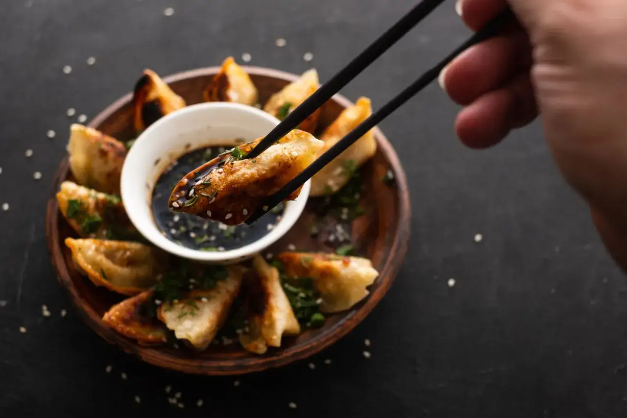 Złociste pierogi gyoza, chrupiące i aromatyczne, zanurzane w sosie.