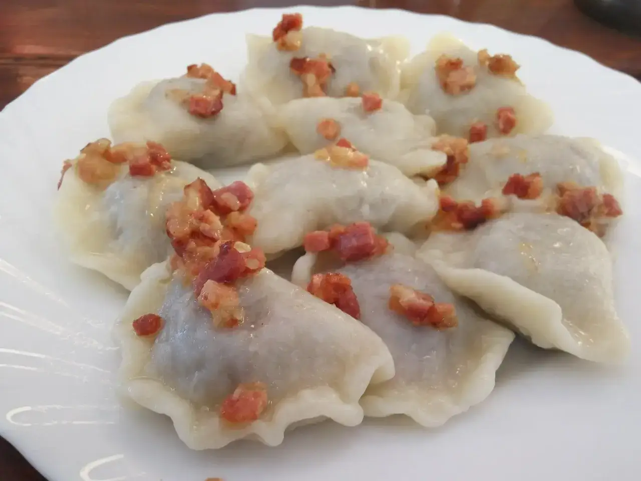 Pyszne pierogi litewskie, okraszone skwarkami, ułożone na białym talerzu.