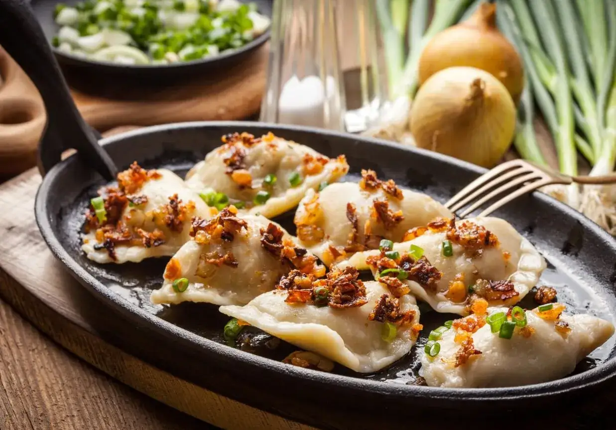 Pyszne pierogi ruskie, okraszone skwarkami i szczypiorkiem, podane na gorącej patelni.