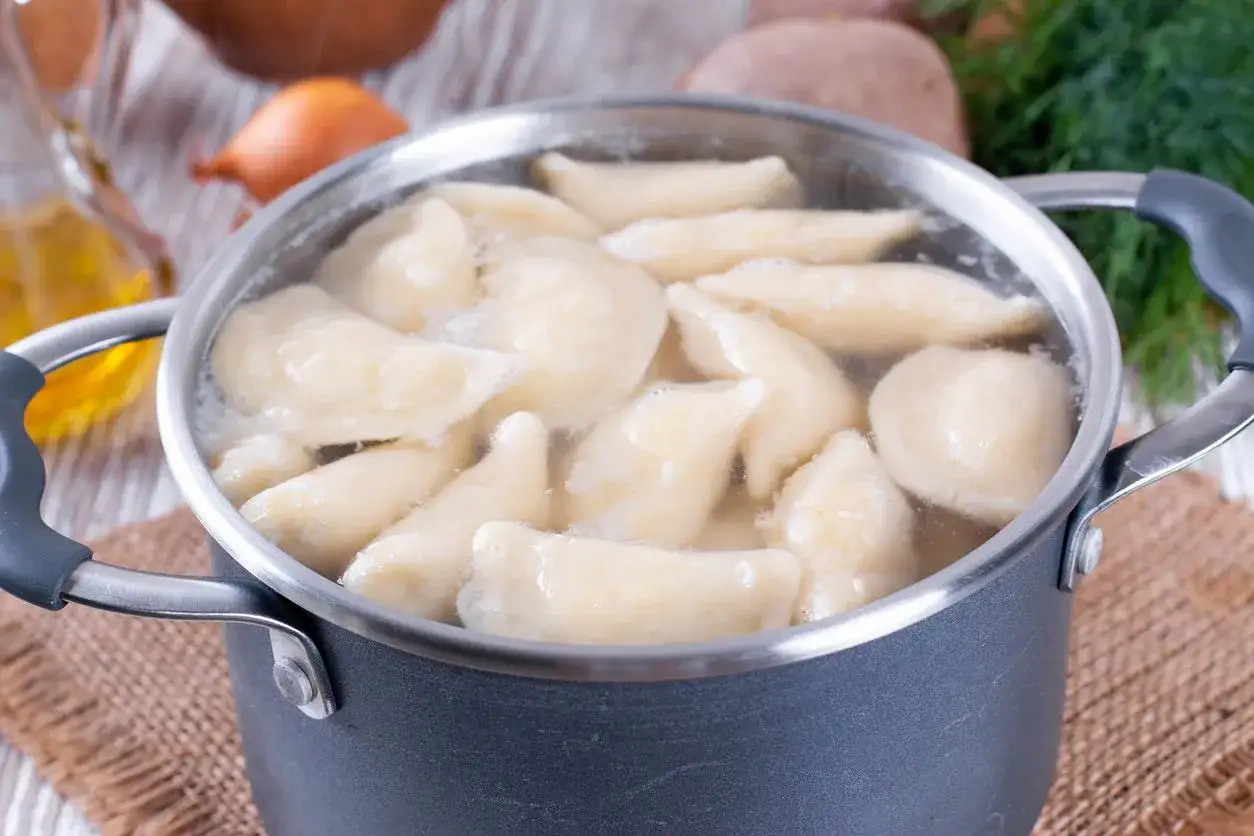 Gotowanie pierogów: gdy wypłyną na powierzchnię, gotuj jeszcze 2-3 minuty. W garnku bulgoczą pierogi, obok cebula i koperek.