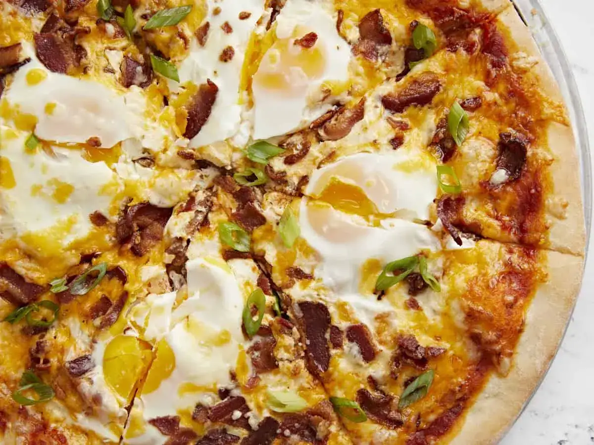 Pyszna pizza z jajkiem, chrupiącym boczkiem i zieloną cebulką. Idealna na śniadanie lub brunch.